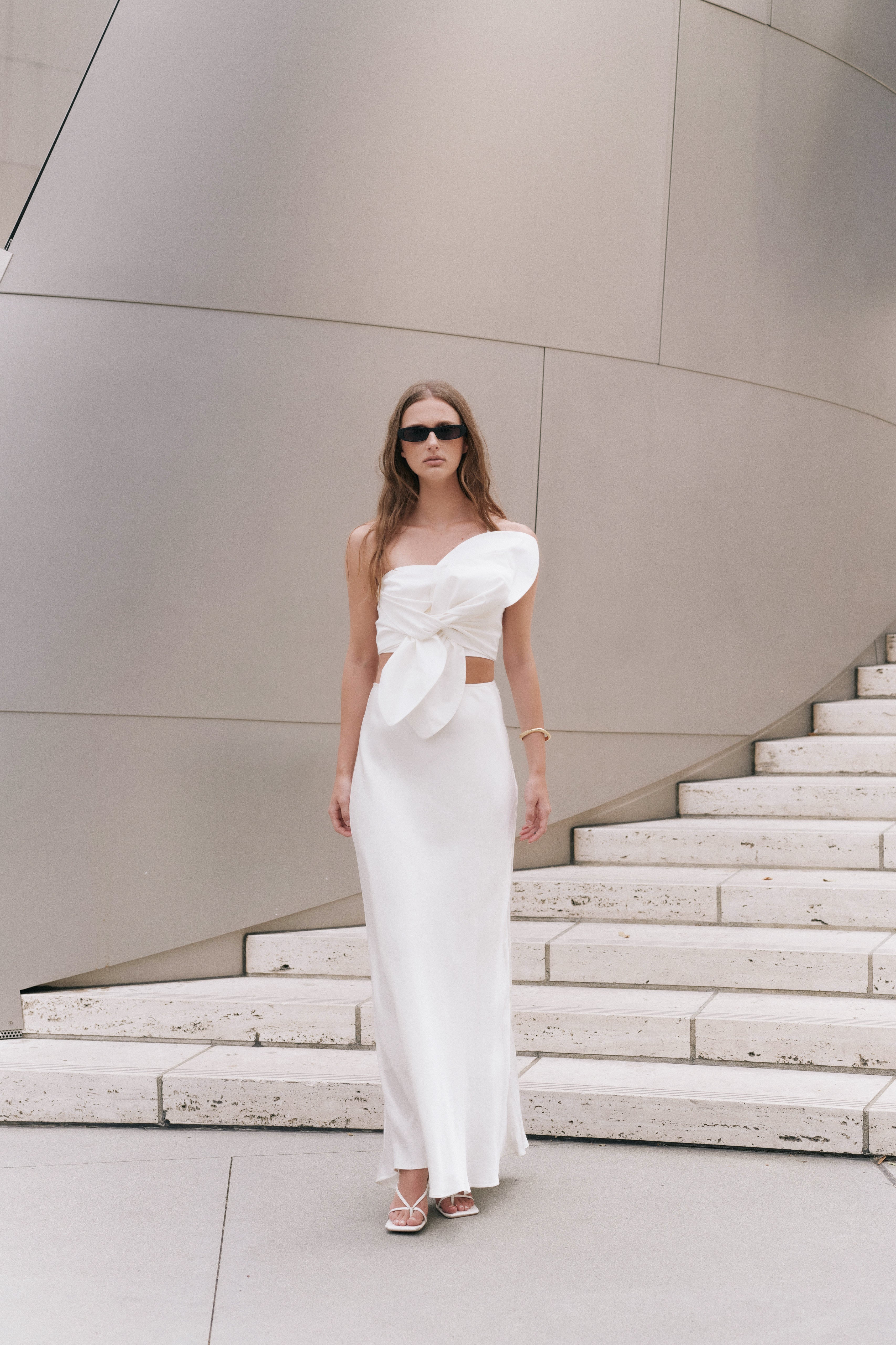 Full-length front view of an off-white strapless crop top featuring a sculptural oversized front knot bow detail.