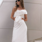 Three-quarter close-up view of an off-white strapless crop top highlighting the large sculptural front knot bow.