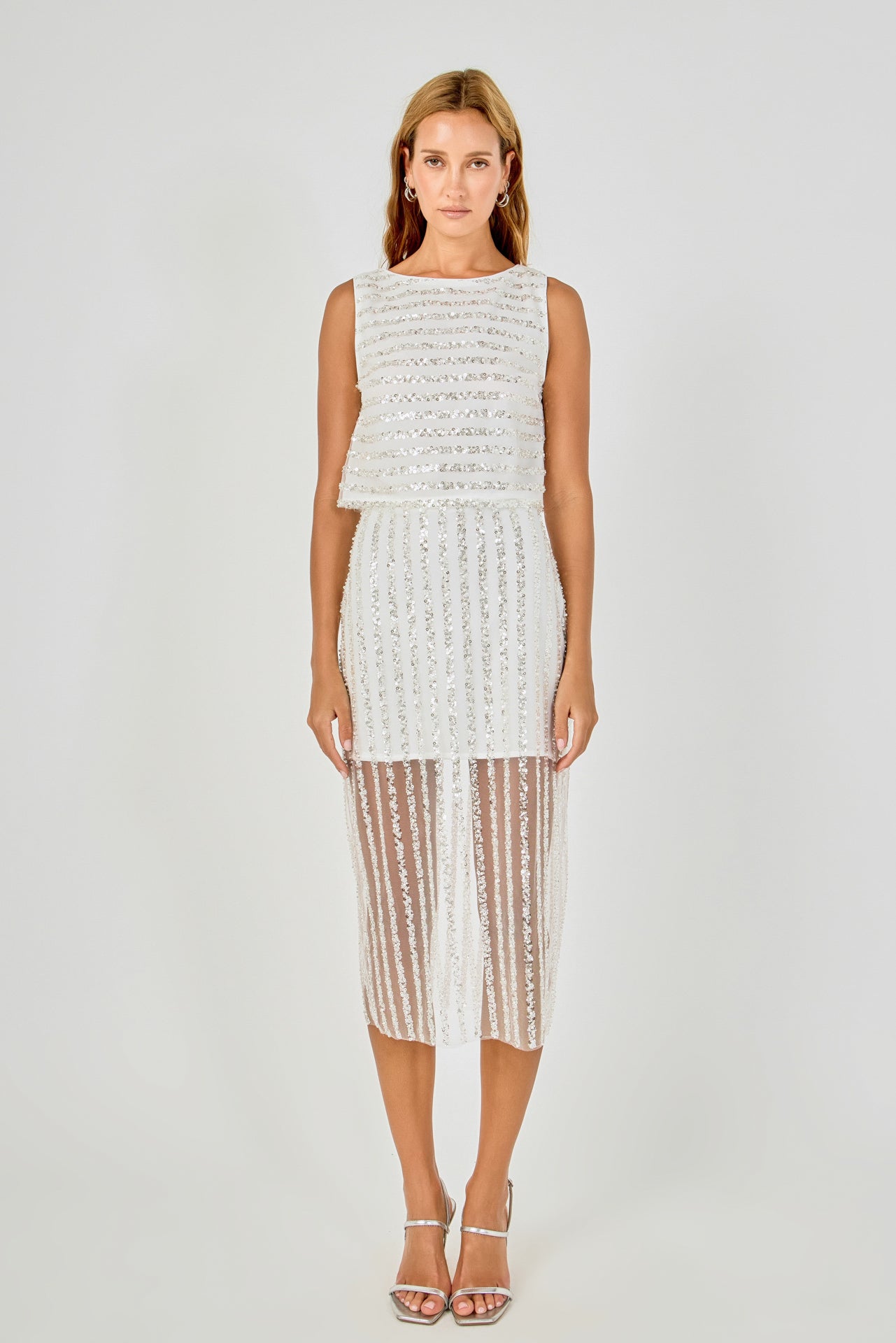 Full-length front view of an off-white sleeveless sequin crop top featuring horizontal sequin stripes and a cropped hem, styled with a matching vertical sequin stripe sheer mesh midi skirt.