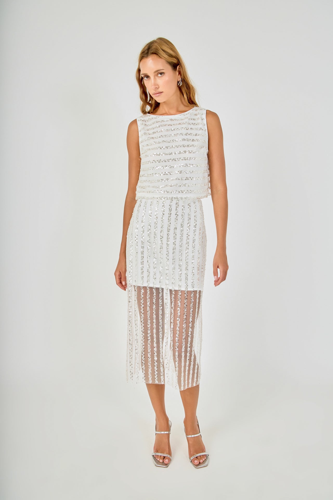 Face-forward posed view of an off-white sleeveless sequin crop top and matching sequin stripe sheer mesh midi skirt, showcasing the full ensemble in a clean front-facing pose.