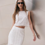 Upper body close-up view of an off-white sleeveless crop top highlighting the high neckline and horizontal sequin stripe pattern.