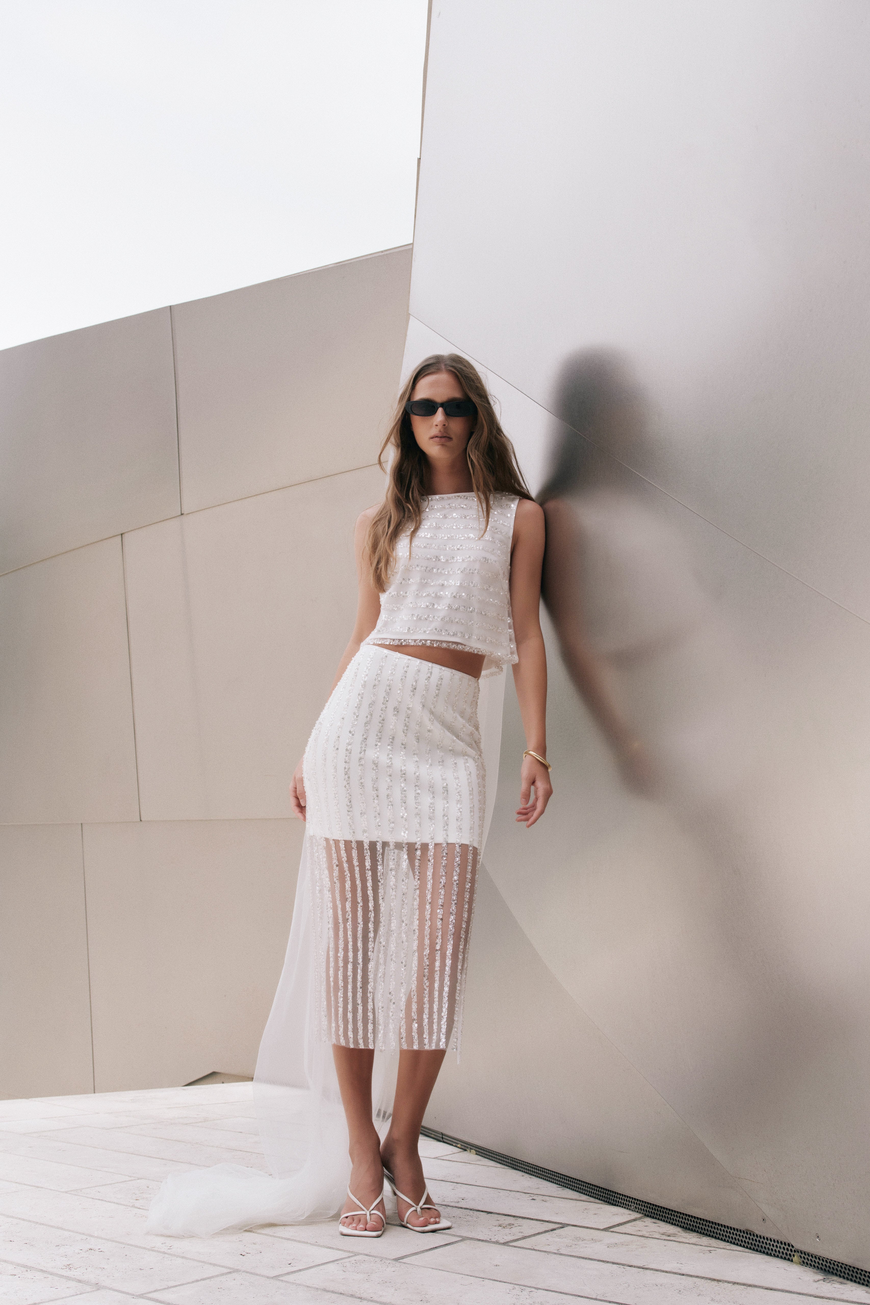 Full-length view of an off-white sleeveless crop top featuring horizontal sequin stripes, styled with a matching sequin skirt.