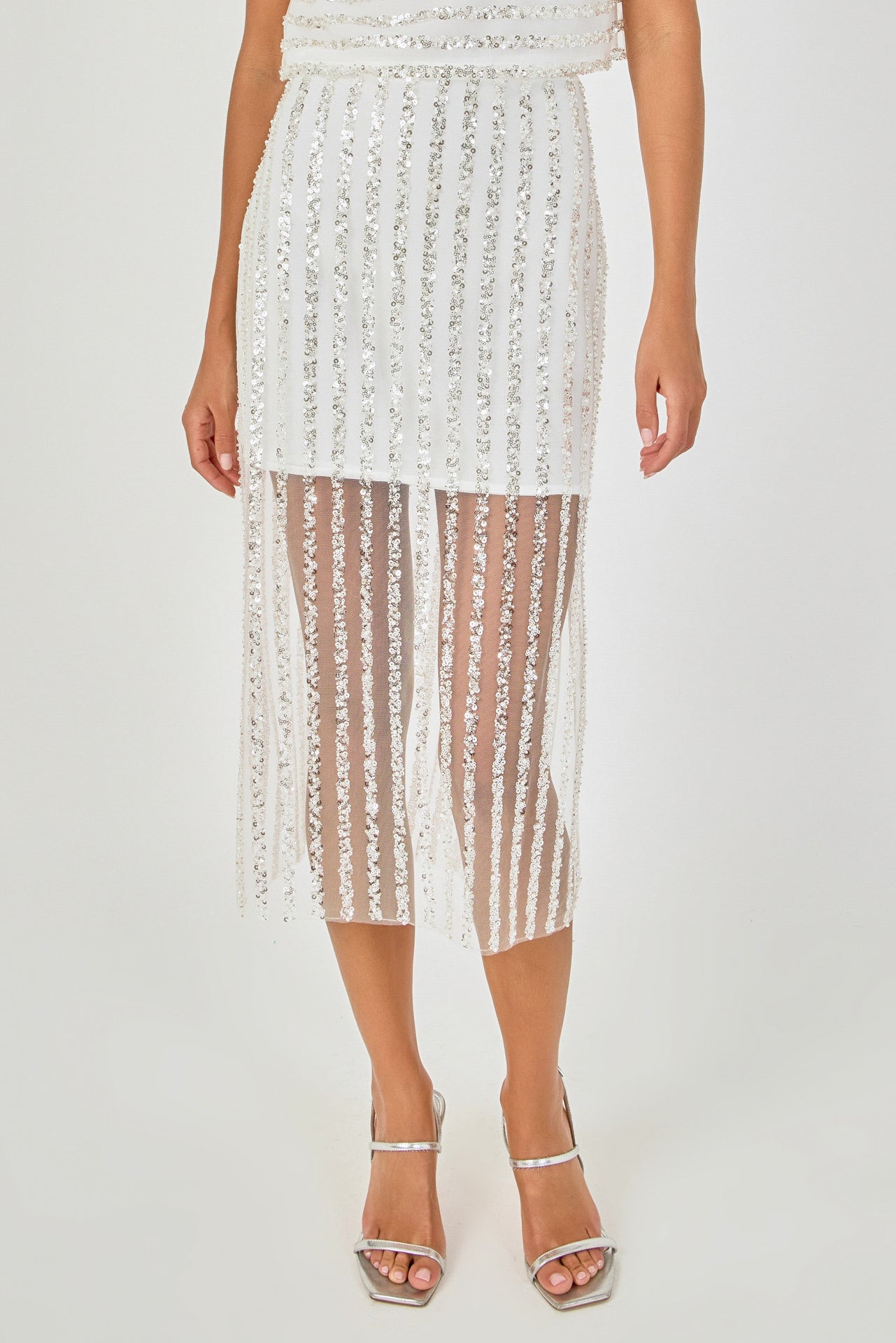 Close-up view of an off-white sequin stripe mesh midi skirt highlighting the sheer mesh hem panel, mini skirt lining, and vertical sequin embroidery.