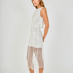 Side posed view of an off-white sequin stripe mesh midi skirt featuring an opaque mini skirt lining and sheer hem, styled with a matching sequin crop top.