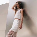 Three-quarter posed view of an off-white sequined midi skirt highlighting the fitted waistline, vertical sequin embellishments, and sheer mesh lower panel with a slit.