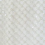 Ultra close-up detail view of white fabric densely embellished with a diamond lattice grid pattern of delicate pearls and tonal sequins.