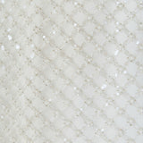 Ultra close-up detail view of white fabric densely embellished with a diamond lattice grid pattern of delicate pearls and tonal sequins.