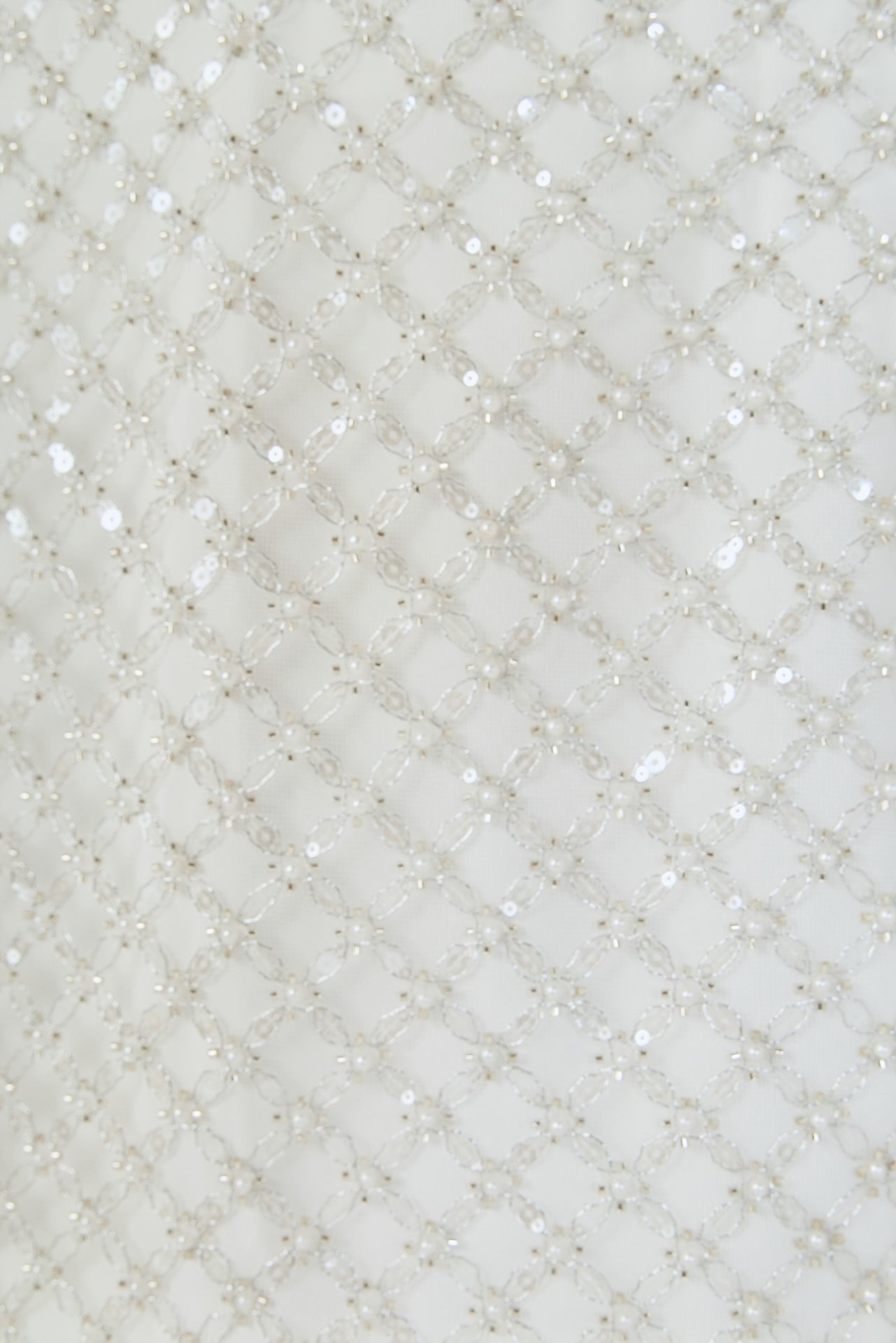 Ultra close-up detail view of white fabric densely embellished with a diamond lattice grid pattern of delicate pearls and tonal sequins.