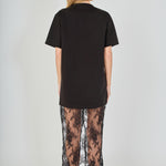Back view of black mix media maxi dress featuring a short-sleeve t-shirt bodice, sheer floral lace skirt, and a back slit.