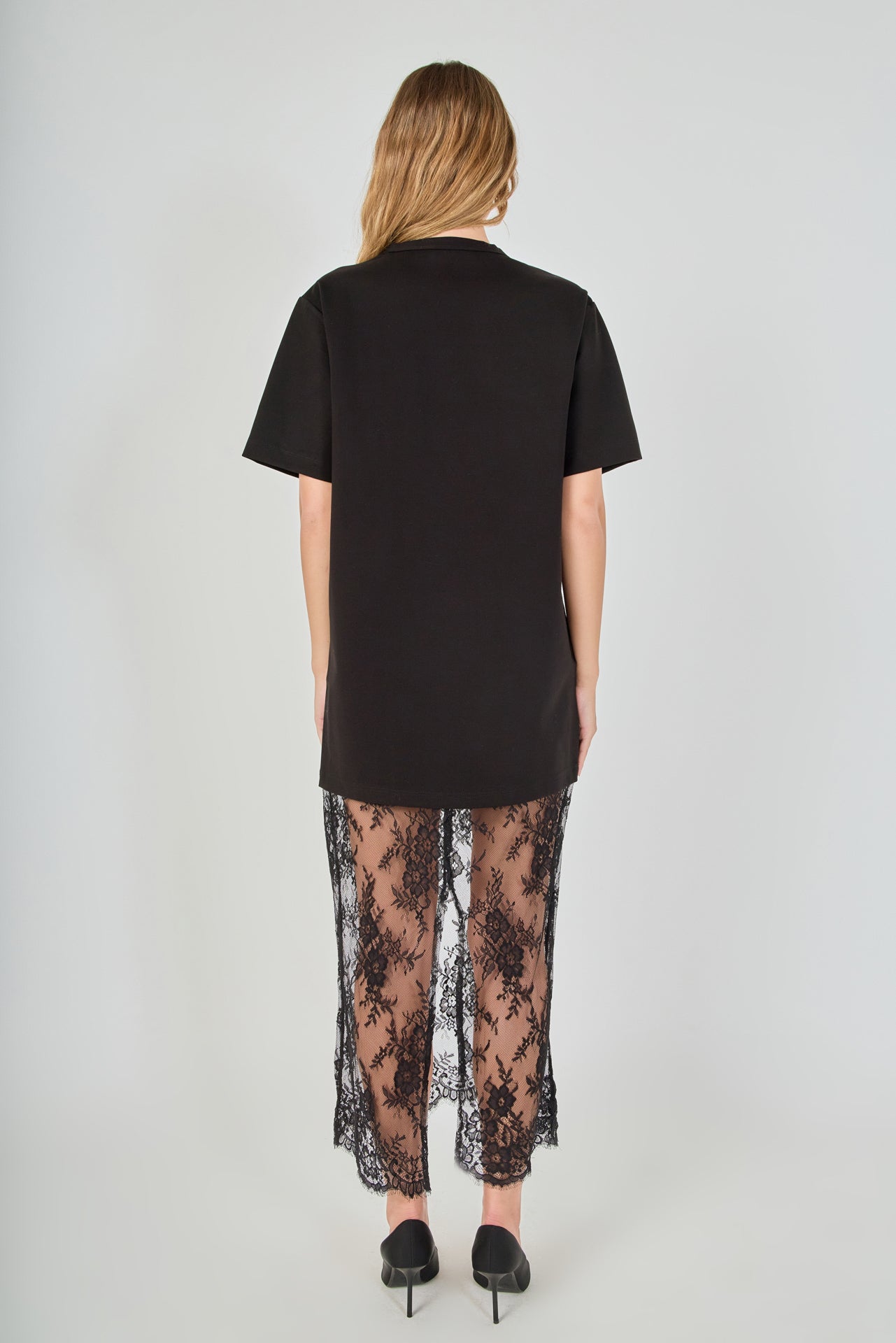 Back view of black mix media maxi dress featuring a short-sleeve t-shirt bodice, sheer floral lace skirt, and a back slit.
