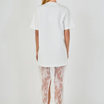 Back view of white mix media maxi dress featuring a short-sleeve t-shirt bodice, sheer floral lace skirt, and a back slit.