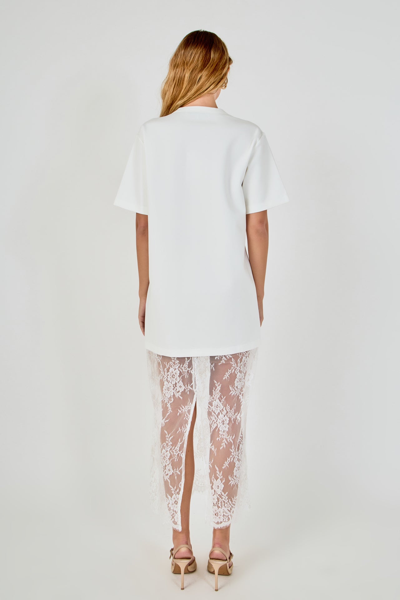 Back view of white mix media maxi dress featuring a short-sleeve t-shirt bodice, sheer floral lace skirt, and a back slit.
