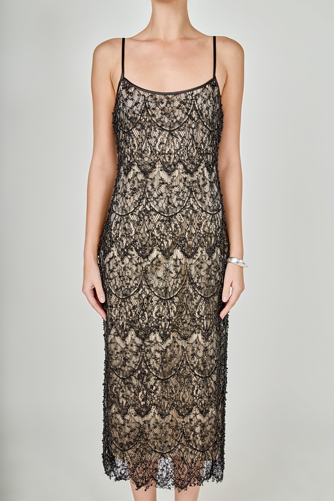 Close-up view of black beaded lace midi dress featuring thin spaghetti straps, a scoop neckline, and a nude inner lining.