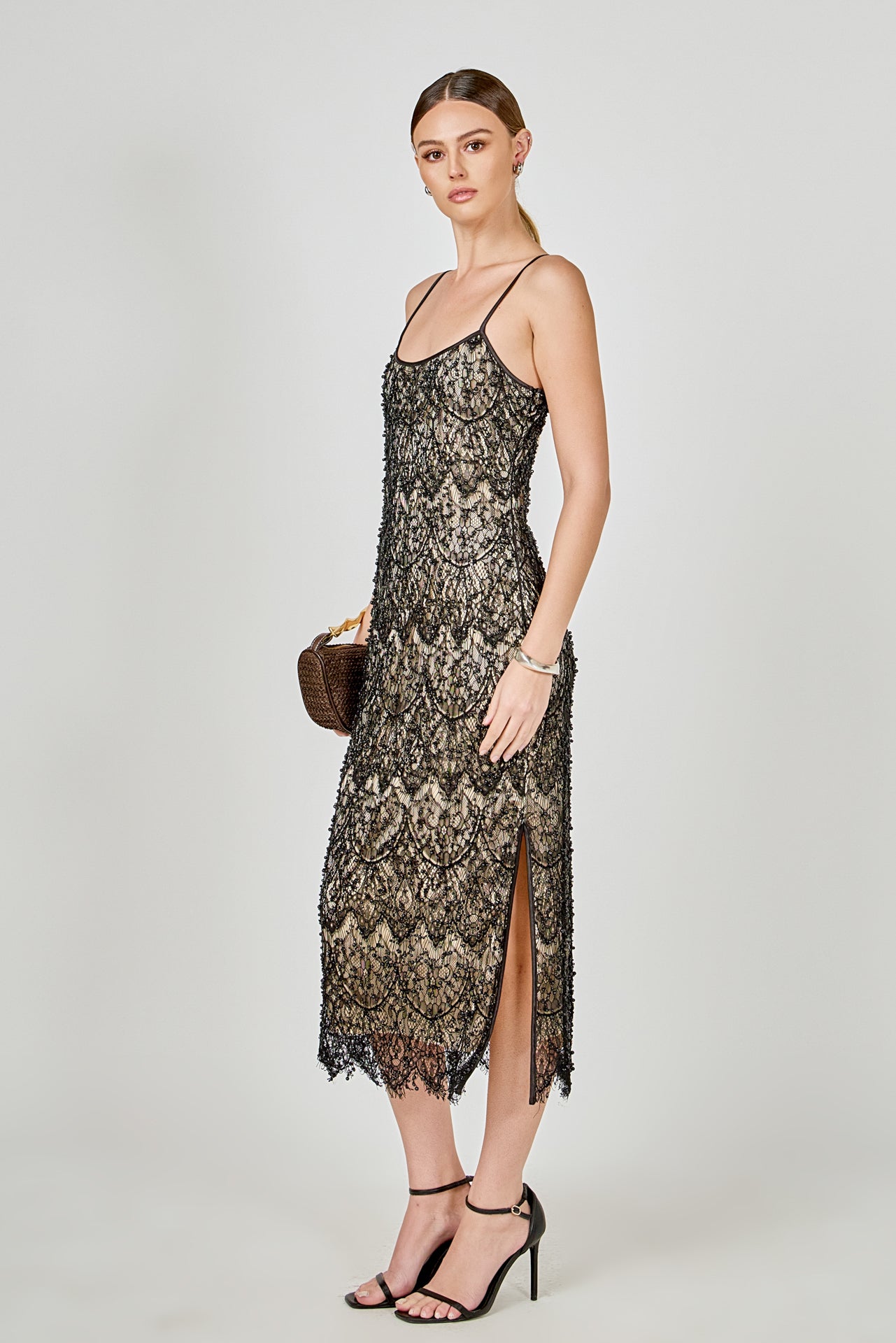 Side view of black beaded lace midi dress featuring thin spaghetti straps, a fitted silhouette, and a side slit.
