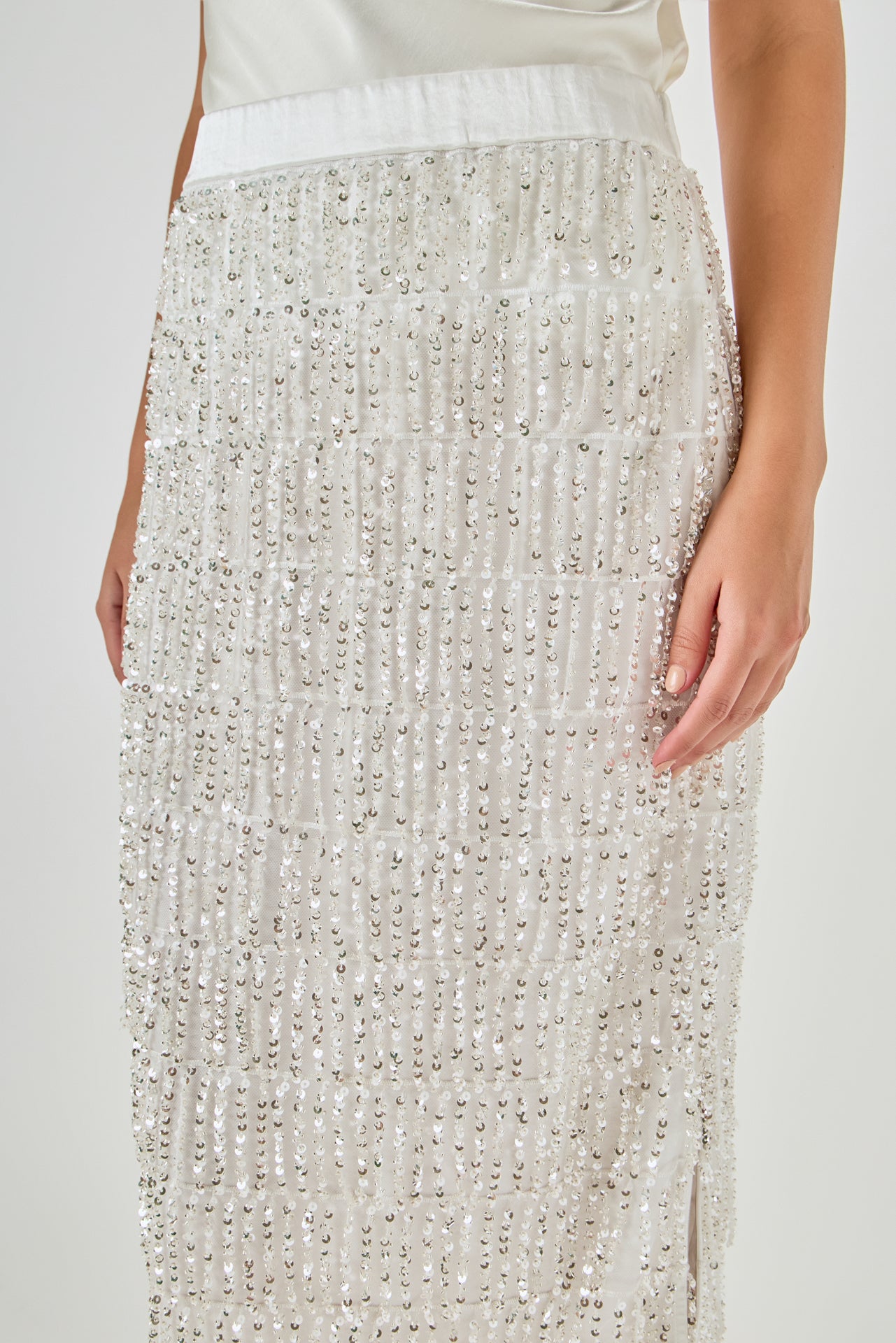 Close-up view of white sequin fringe midi skirt highlighting the smooth satin waistband and upper tiered sequin detailing.