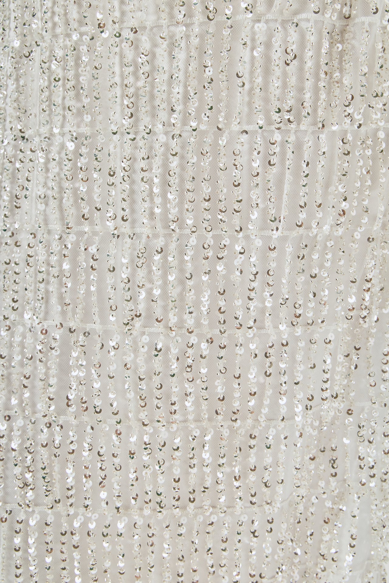 Ultra close-up detail view of white mesh fabric densely embroidered with tiered rows of shimmering metallic sequin fringe.