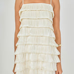 Close-up view of cream tiered bubble mini dress highlighting the straight neckline, thin adjustable straps, and upper pleated layers.