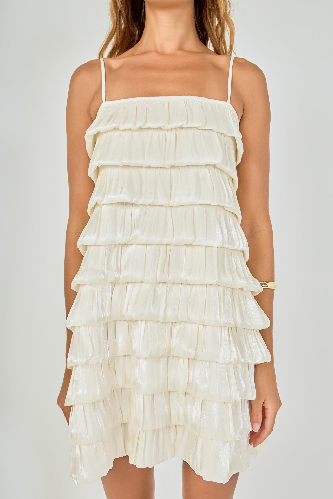 Close-up view of cream tiered bubble mini dress highlighting the straight neckline, thin adjustable straps, and upper pleated layers.