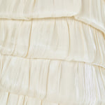 Ultra close-up detail view of cream pleated fabric arranged in textured, overlapping ruffled bubble tiers.