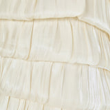 Ultra close-up detail view of cream pleated fabric arranged in textured, overlapping ruffled bubble tiers.