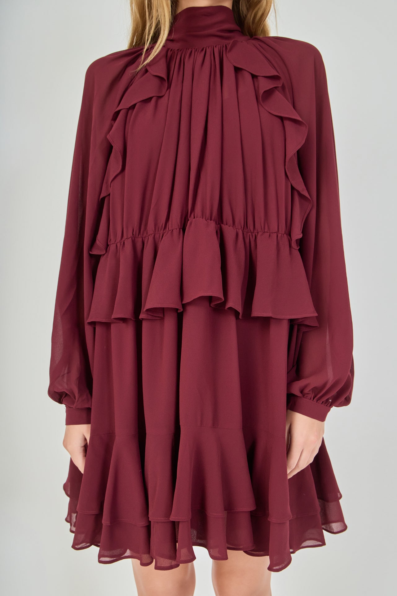Zoomed-in view focusing on the chest, detailing the smocked high collar, the sheer fabric of the bishop sleeves, and the complex vertical cascading ruffles that frame the bodice.