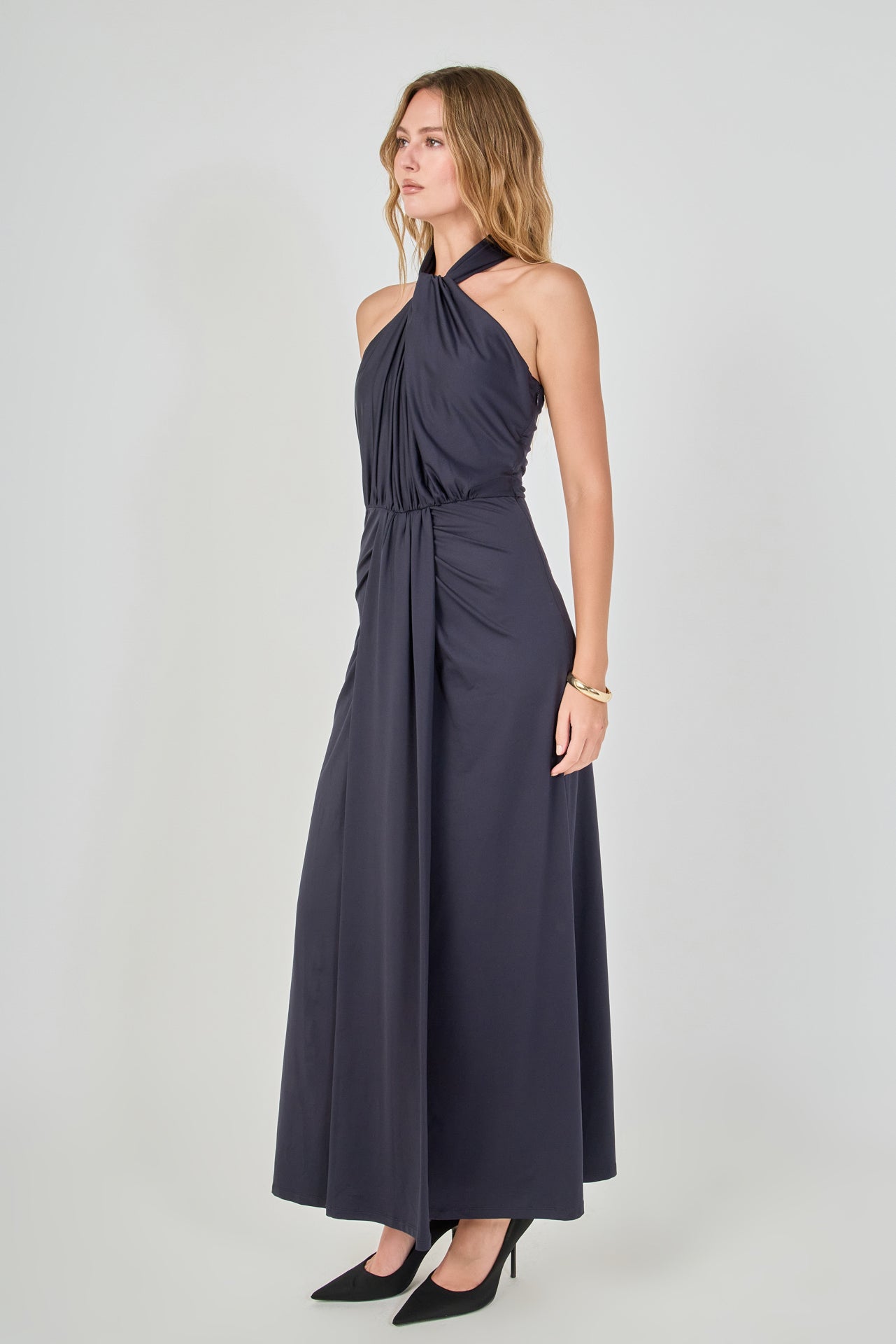 Side view of navy draped halter maxi dress featuring a high halter neckline, front drape detail, and a fluid maxi skirt.