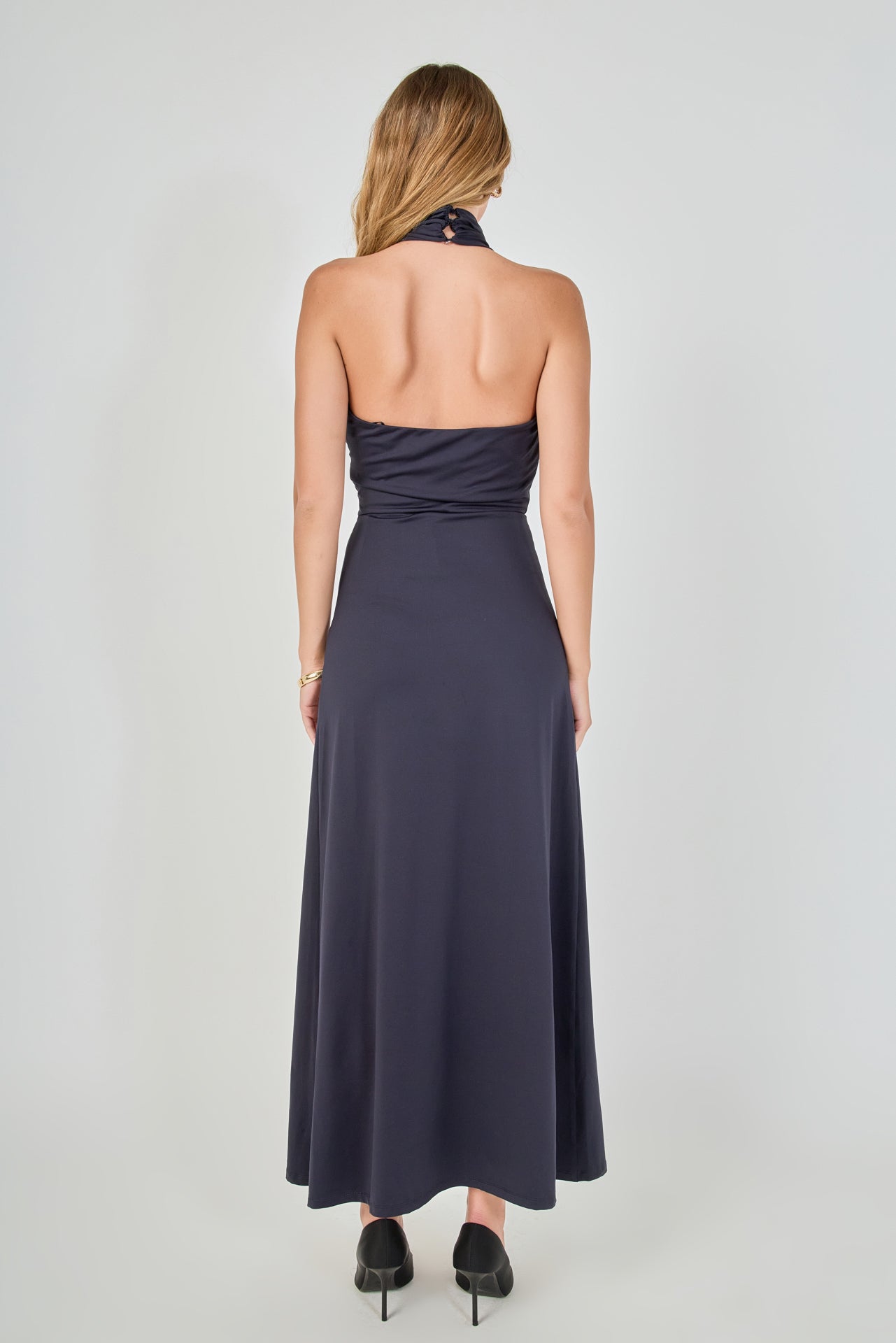 Back view of navy draped halter maxi dress featuring a high halter neck, open back design, and a floor-length hem.