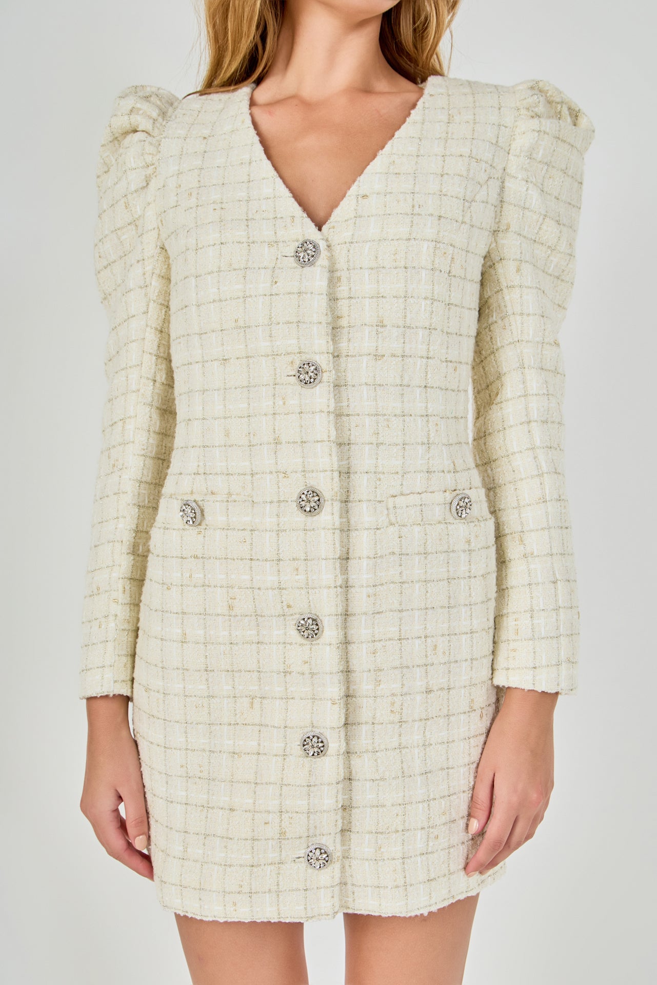 Upper bodice close-up view of an ivory windowpane tweed mini dress highlighting the V-neckline, puffed sleeve caps, and decorative crystal buttons.