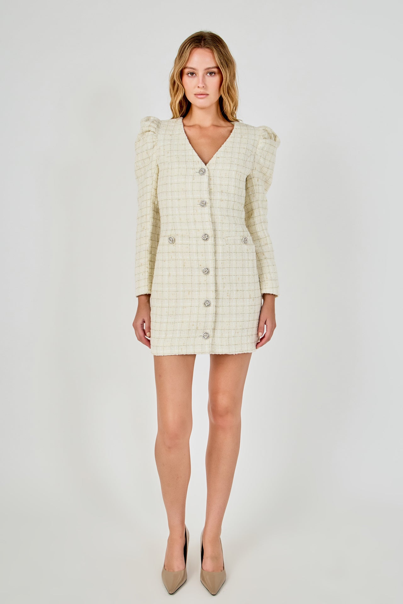 Full-length front view of an ivory long-sleeve tweed mini dress with structured puff shoulders, a central crystal button placket, and front flap accents.