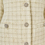 Ultra close-up detail view of ivory woven tweed fabric featuring a subtle gold metallic windowpane grid, ornate crystal floral buttons, and faux flap pockets.