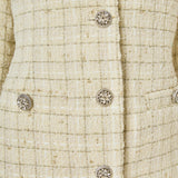 Ultra close-up detail view of ivory woven tweed fabric featuring a subtle gold metallic windowpane grid, ornate crystal floral buttons, and faux flap pockets.