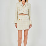 Full-length front view of an ivory high-waisted tweed mini skirt styled with a matching long-sleeve cropped blazer set.