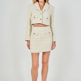 Full-length front view of an ivory high-waisted tweed mini skirt styled with a matching long-sleeve cropped blazer set.
