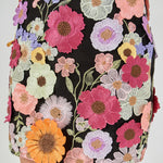 Detail view of black skirt fabric featuring dense multi-colored floral embroidery in vibrant shades of pink, orange, yellow, mint green, and lavender.