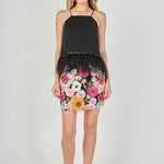 Black floral embroidered mini skirt featuring vibrant multi-colored flower embroidery, a high waist, and a straight hem, styled with a black feather-trimmed camisole top.