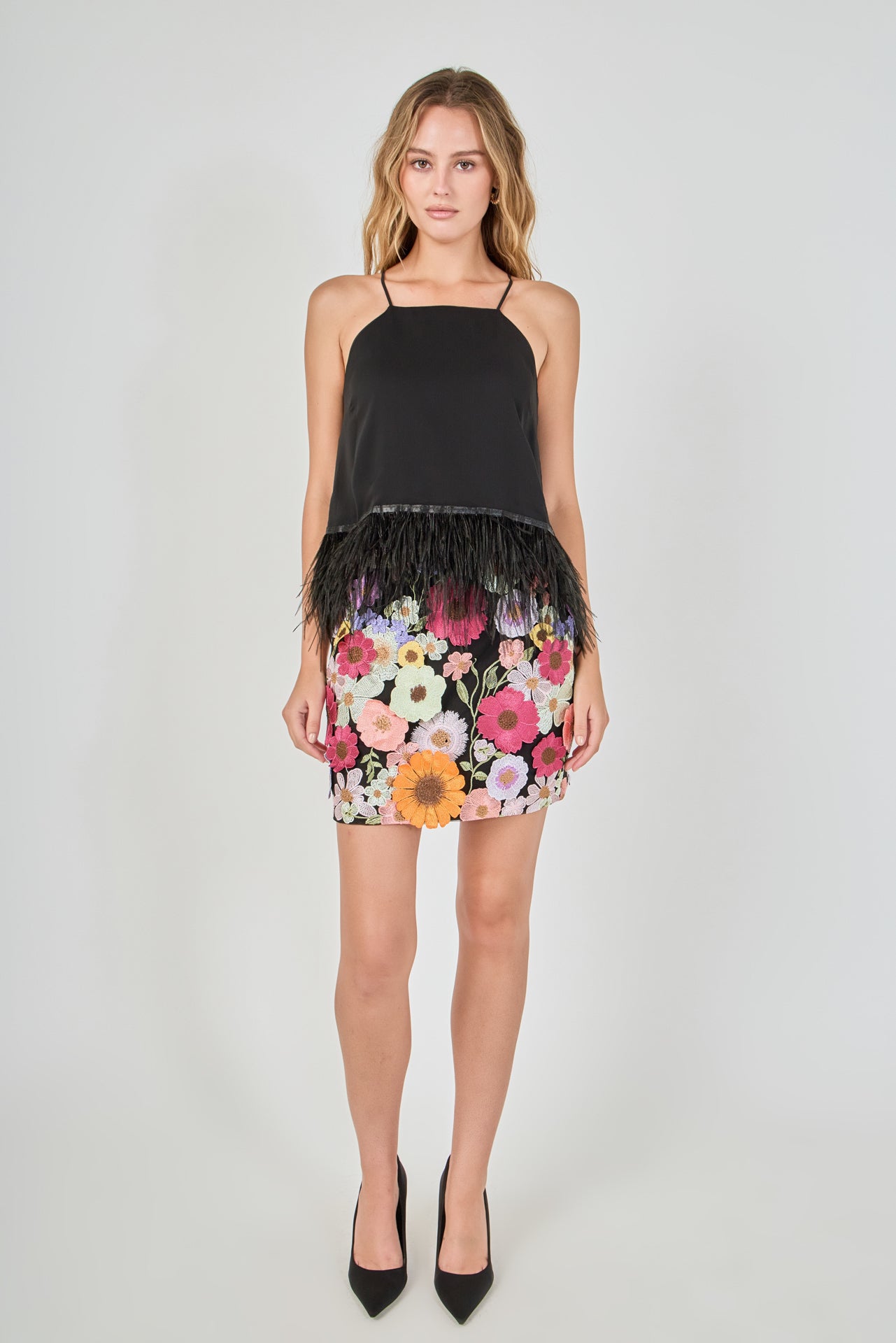 Black floral embroidered mini skirt featuring vibrant multi-colored flower embroidery, a high waist, and a straight hem, styled with a black feather-trimmed camisole top.