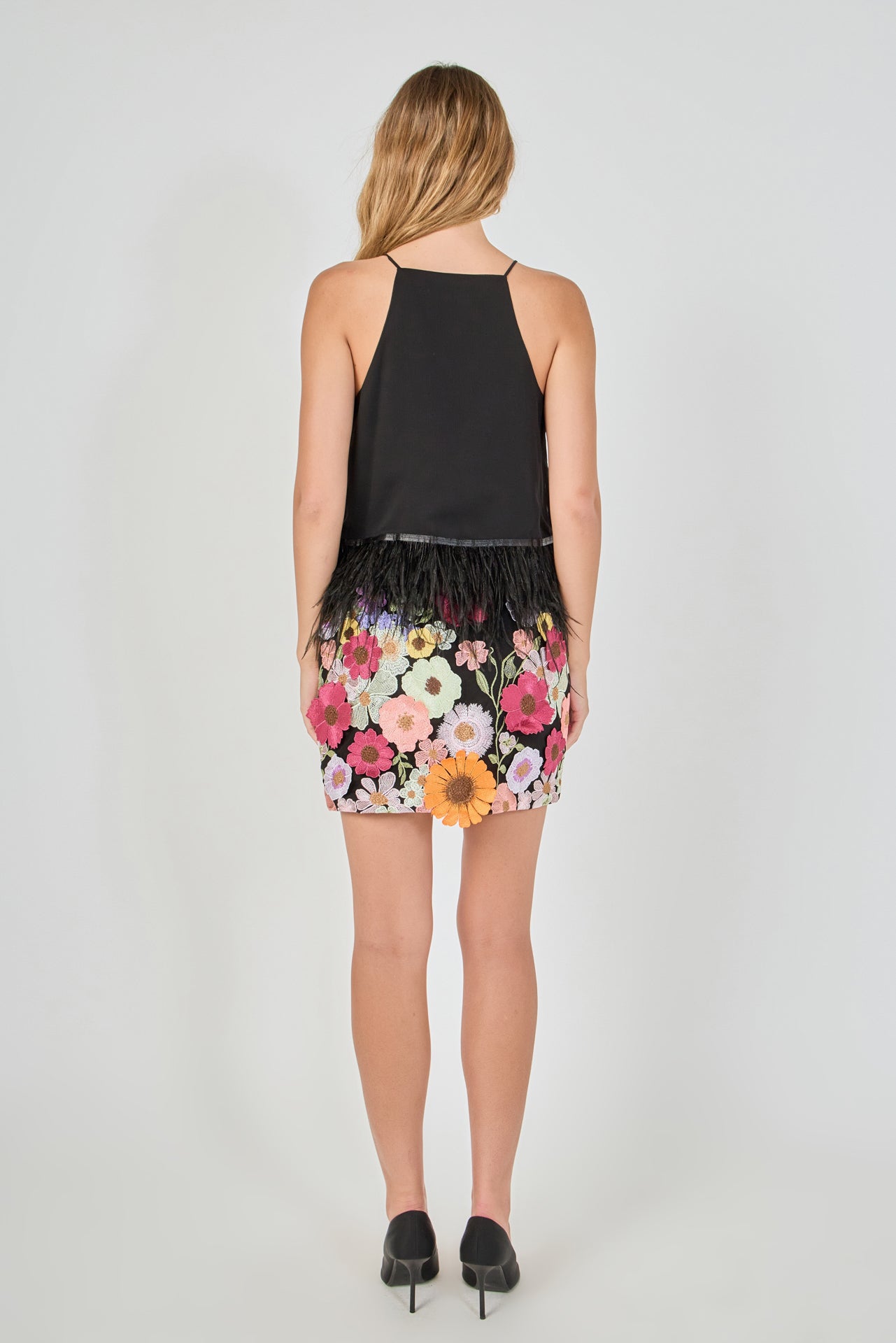 Back view of black floral embroidered mini skirt featuring all-over multi-colored flower embroidery and a straight mini hem.