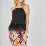 Black floral embroidered mini skirt featuring vibrant multi-colored flower embroidery, a high waist, and a straight hem, styled with a black feather-trimmed camisole top.