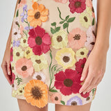 Detail view of beige skirt fabric featuring dense multi-colored floral embroidery in shades of red, orange, yellow, pink, and purple with green stems.