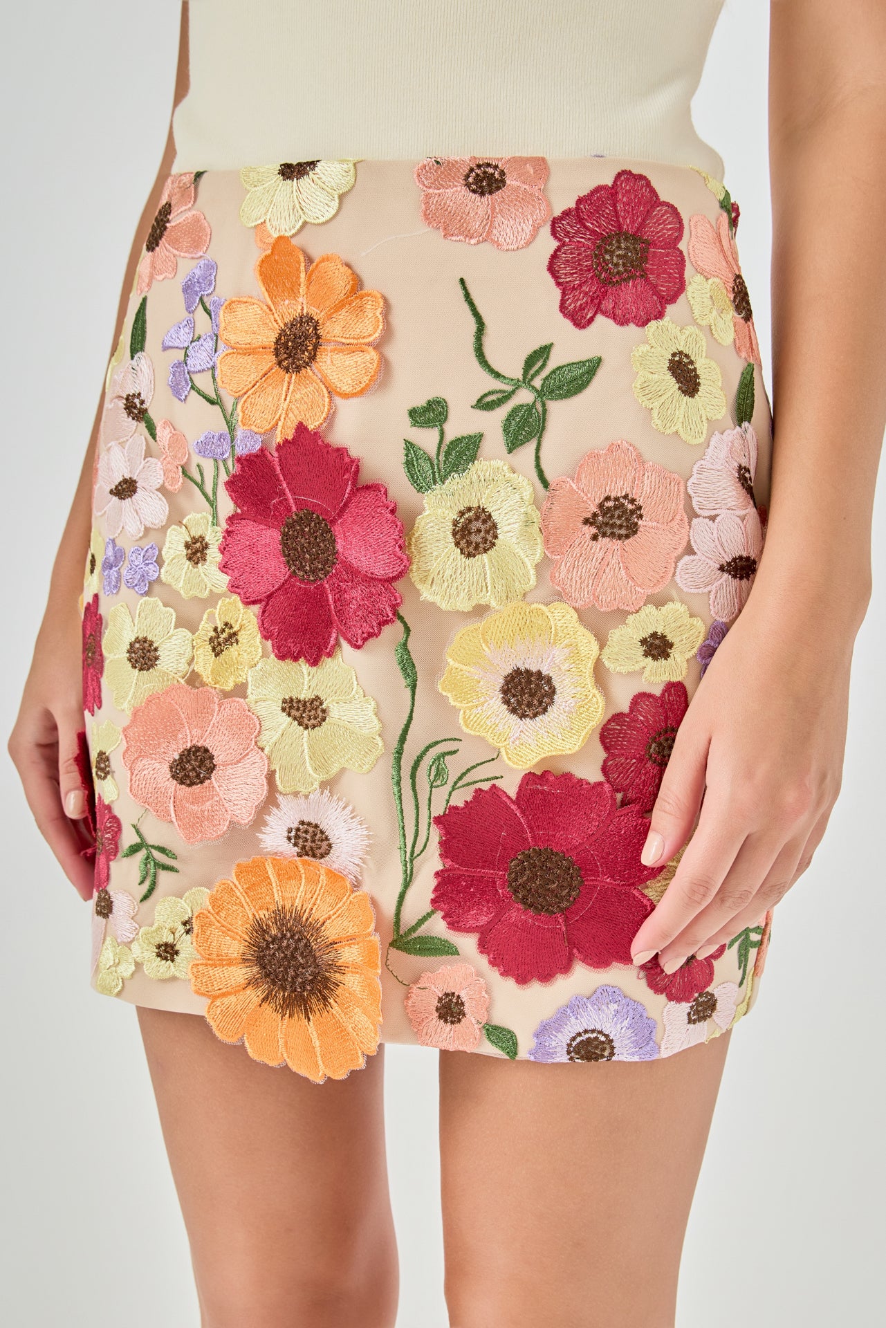 Detail view of beige skirt fabric featuring dense multi-colored floral embroidery in shades of red, orange, yellow, pink, and purple with green stems.
