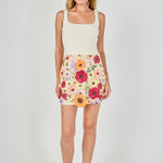 Beige floral embroidered mini skirt featuring dense multi-colored flower embroidery, a high waist, and a straight hem, styled with a cream tank top.