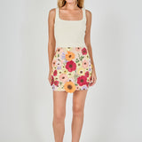 Beige floral embroidered mini skirt featuring dense multi-colored flower embroidery, a high waist, and a straight hem, styled with a cream tank top.