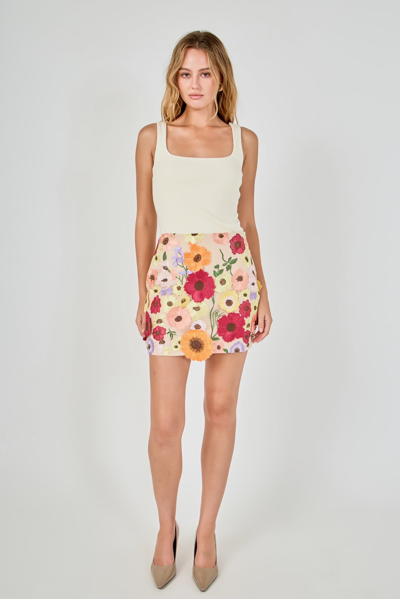 Beige floral embroidered mini skirt featuring dense multi-colored flower embroidery, a high waist, and a straight hem, styled with a cream tank top.