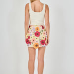 Back view of beige floral embroidered mini skirt featuring multi-colored floral embroidery and a fitted mini hem.