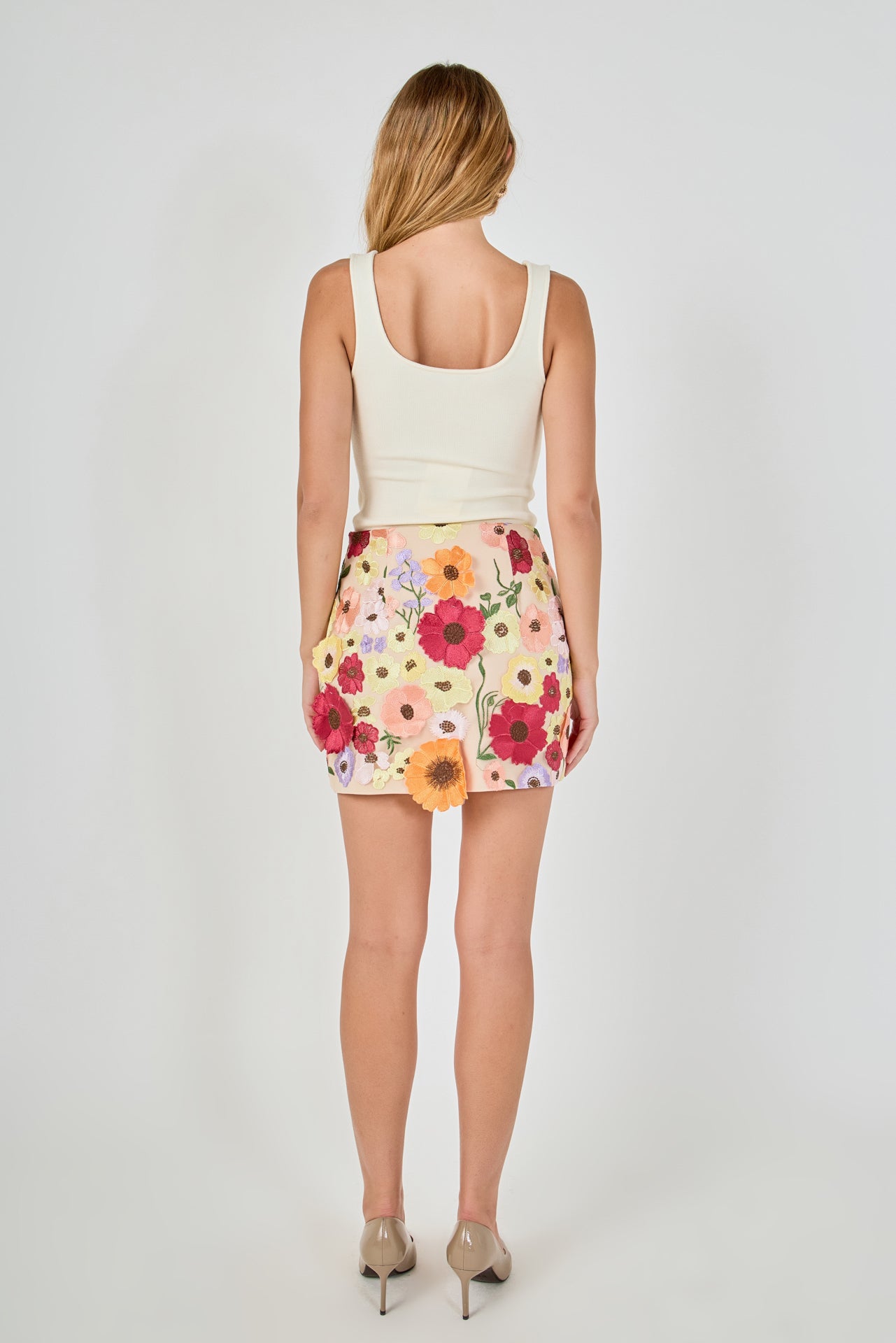 Back view of beige floral embroidered mini skirt featuring multi-colored floral embroidery and a fitted mini hem.