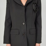 Close-up view of a black blazer highlighting the notch lapel, large intricate 3D rose appliqué, and textured fabric.