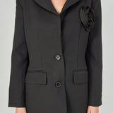 Close-up view of a black blazer highlighting the notch lapel, large intricate 3D rose appliqué, and textured fabric.