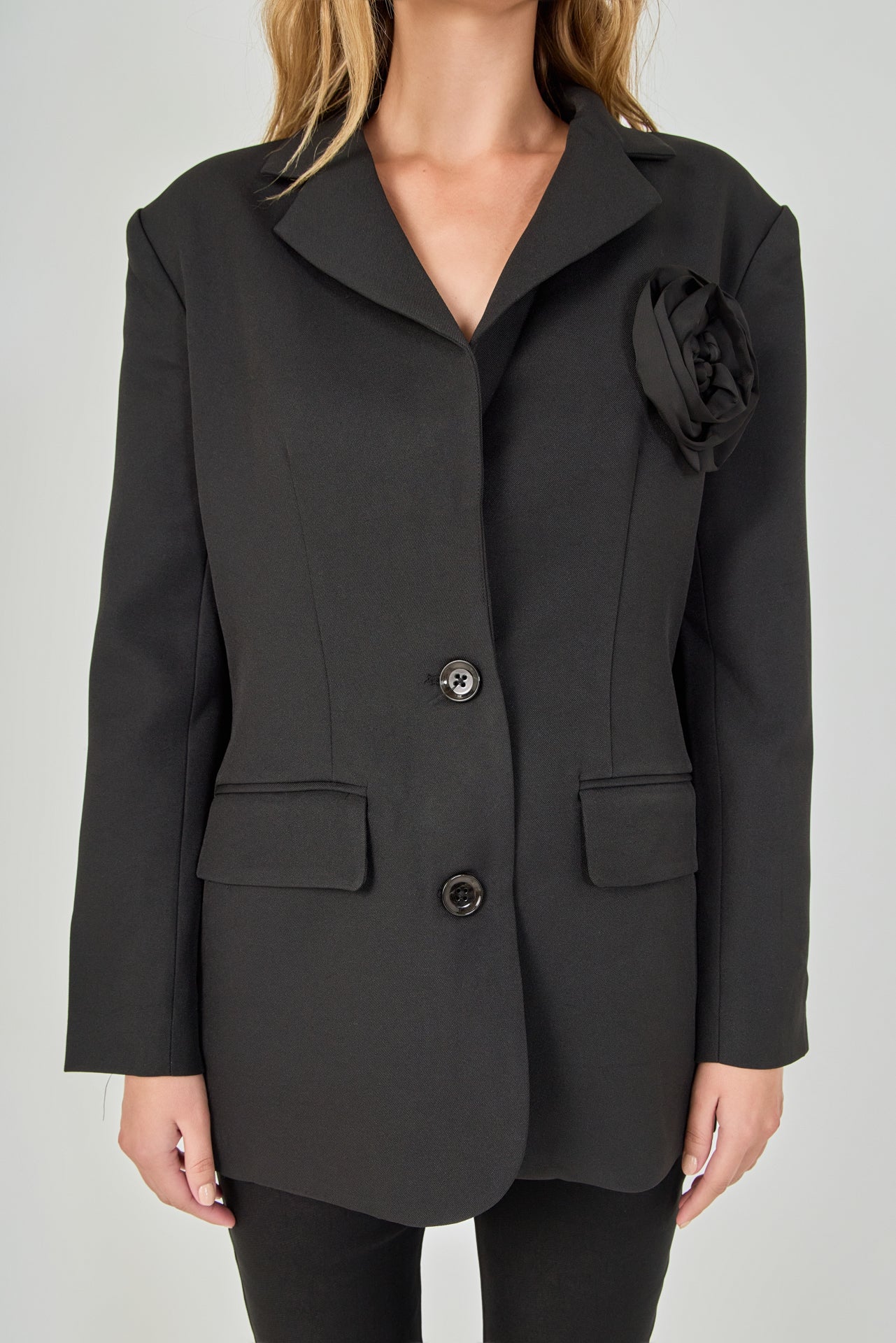 Close-up view of a black blazer highlighting the notch lapel, large intricate 3D rose appliqué, and textured fabric.