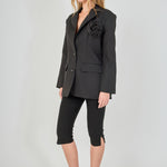 Side view of a black tailored blazer with structural shoulders and a straight hem, paired with fitted black capri pants showing the side-split detail.