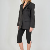 Side view of a black tailored blazer with structural shoulders and a straight hem, paired with fitted black capri pants showing the side-split detail.